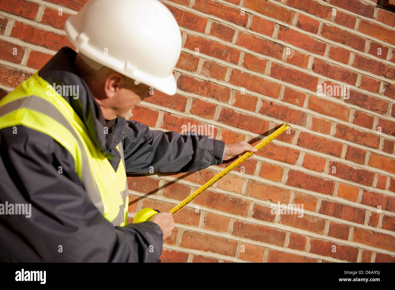 Ispettore edificio prendendo una misura contro un muro di mattoni. Foto Stock