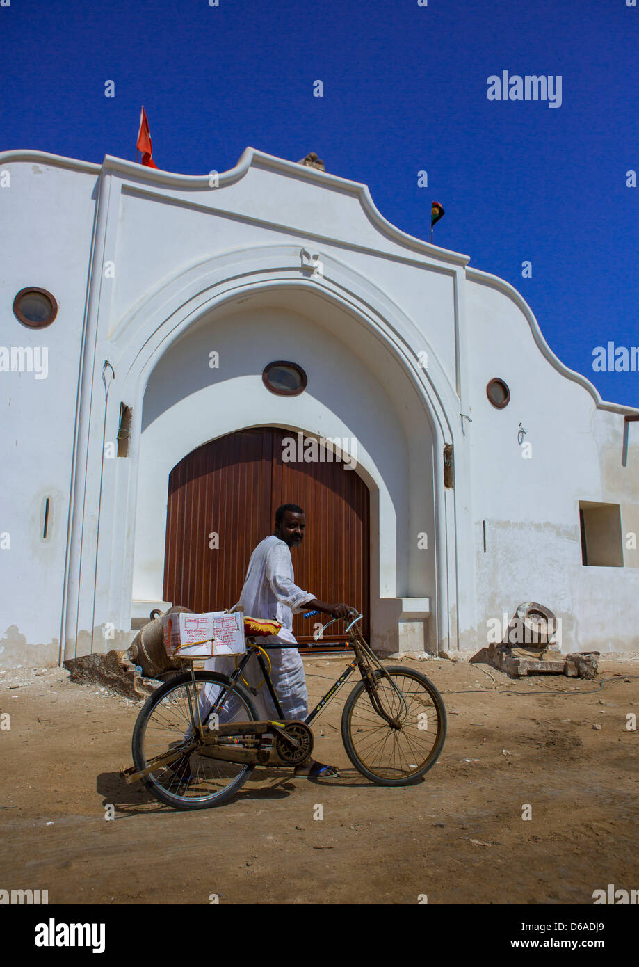 L uomo che passa con la sua bicicletta nella parte anteriore dell'edificio ristrutturato del gateway alla dogana, Suakin, Sudan Foto Stock