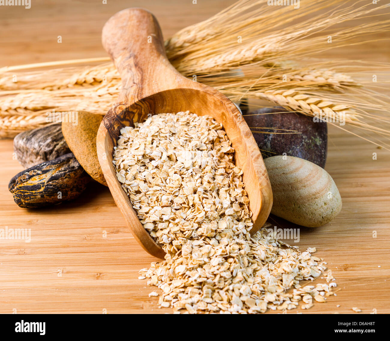 Foto orizzontale di fiocchi d'avena in cucchiaio di legno con pietre rotonde e steli di grano in bamboo naturale il legno Foto Stock