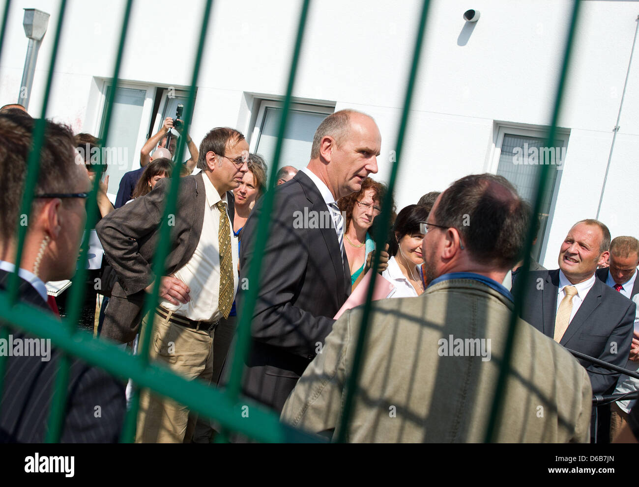 Il Ministro degli Interni del Land di Brandeburgo Dietmar Woidke (L) parla con Uwe Haschmann (R), direttore del Brandeburgo ufficio dell'Ufficio federale per la migrazione e i rifugiati e Stephan Bock (2-L), direttore del Centro di alieni dipartimento di Brandeburgo, dietro una recinzione della nuova struttura di accoglienza per richiedenti asilo della centrale di stranieri" Ufficio Brandeburgo in Schoenefeld, Germania Foto Stock