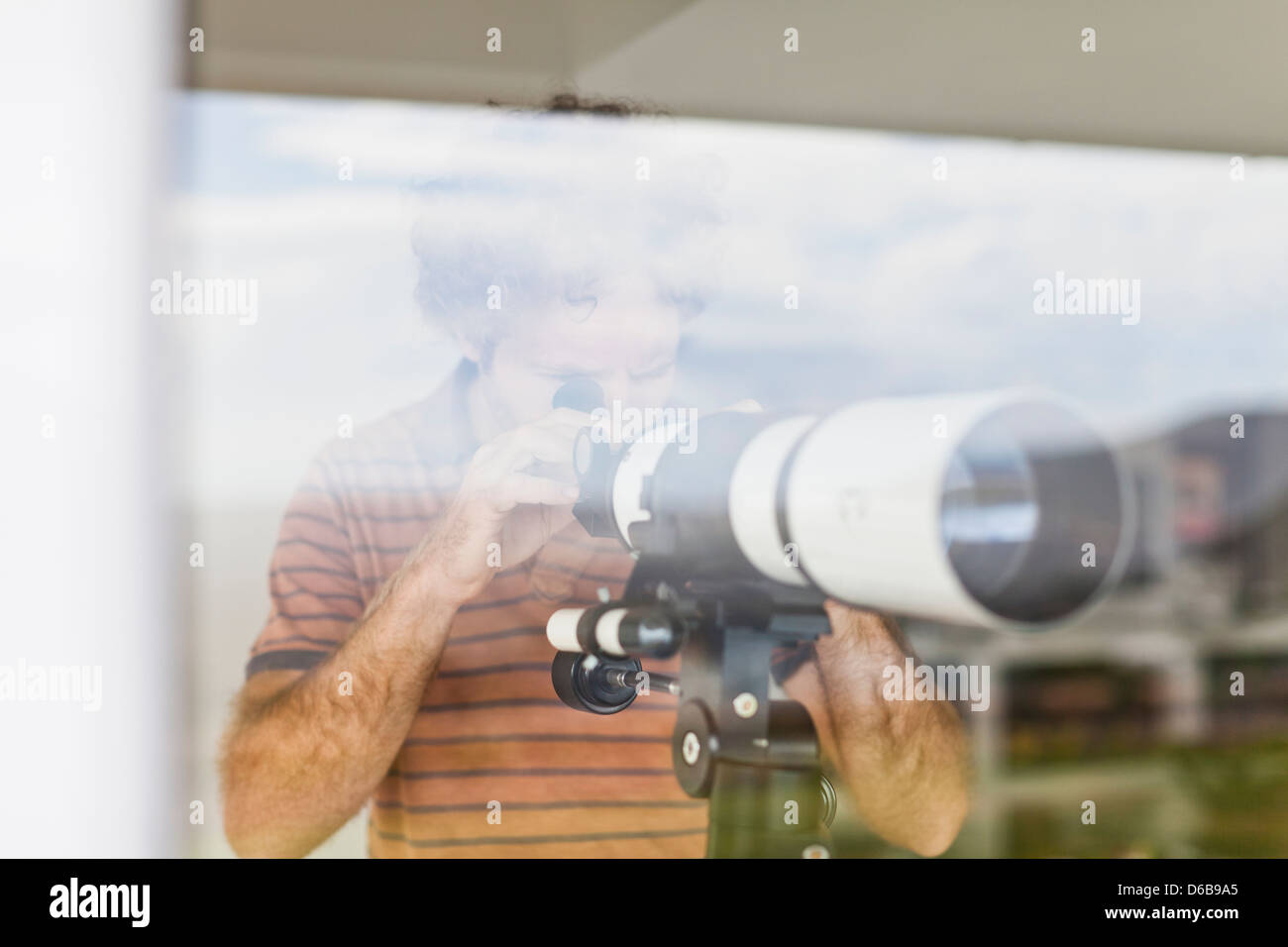 L'uomo utilizzando un telescopio in corrispondenza della finestra Foto Stock