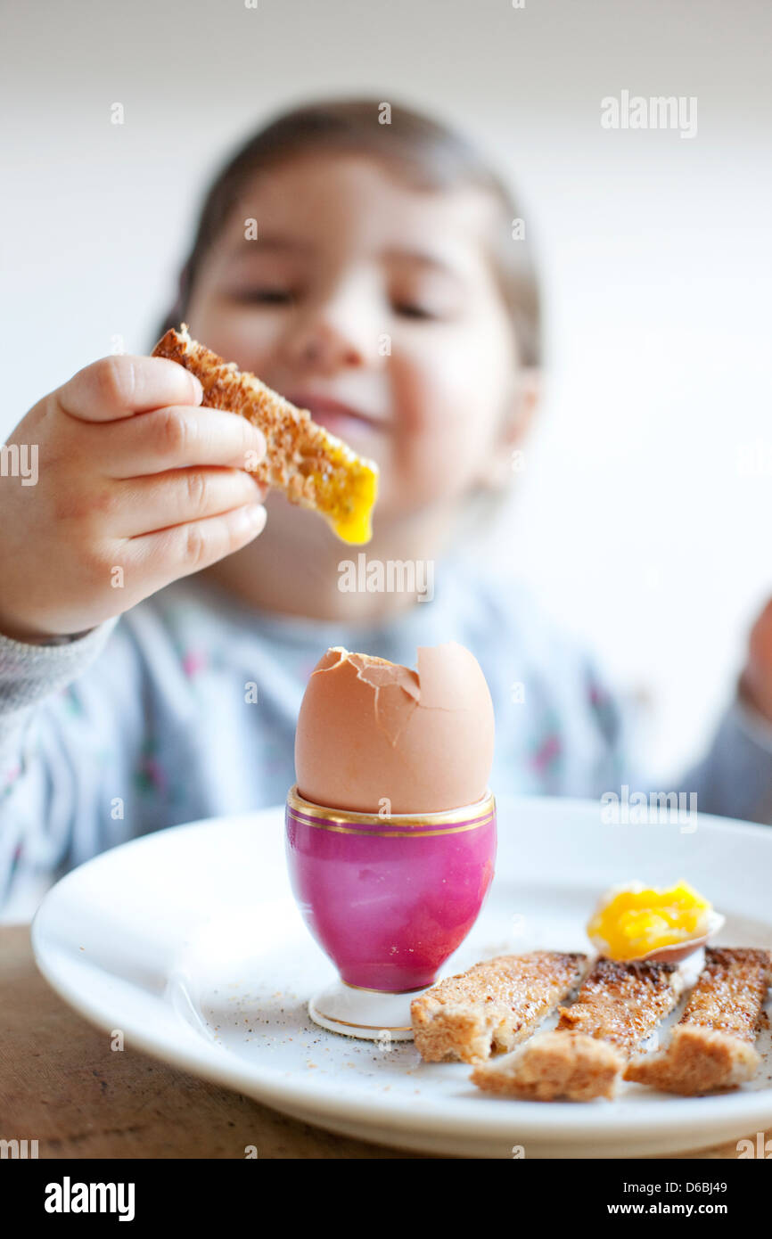 Ragazza dipping toast con le uova a colazione Foto Stock