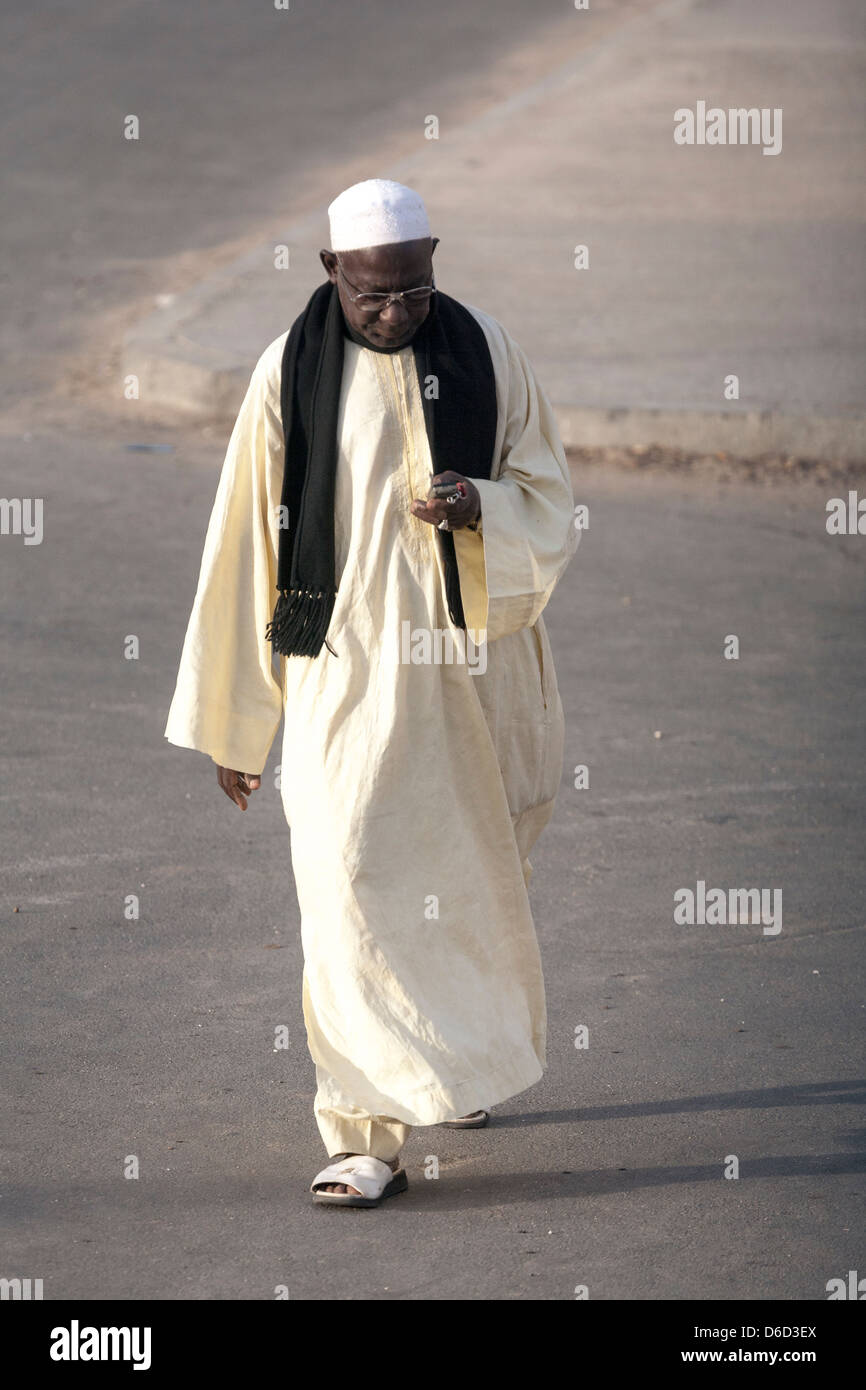 Un vestito uomo senegalesi in costume tradizionale (kaftan senegalesi, boubou o mbubb) percorrendo a piedi e i messaggi di testo con il suo cellulare Foto Stock