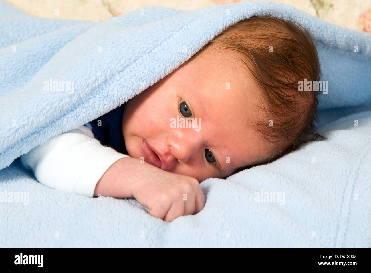 Bella bianca baby boy con grandi occhi è giacente sotto la coperta Foto Stock