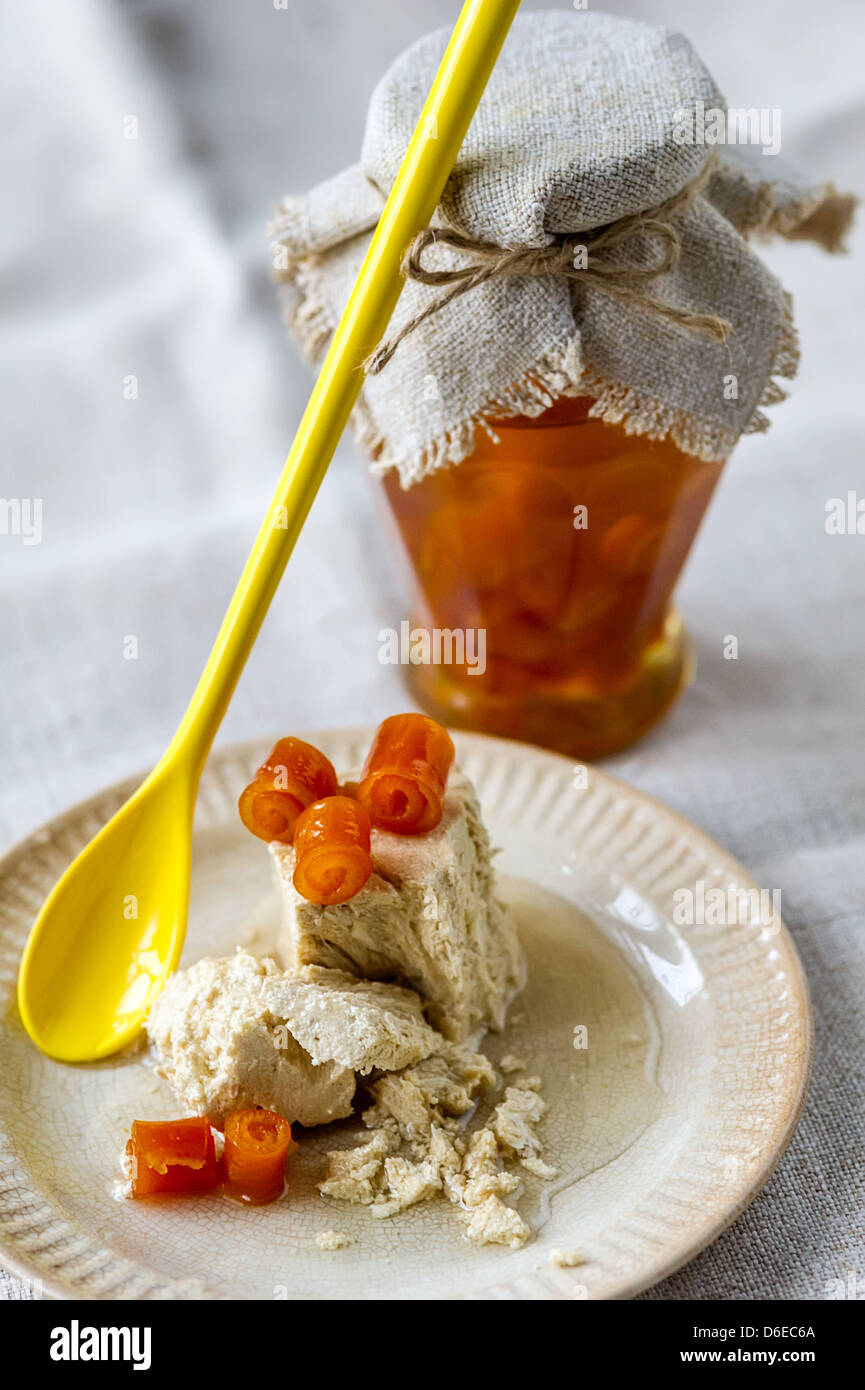 Vaso di vetro di marmellata di arancio, giallo cucchiaio e dolce halva ritorto con bucce di arancia su una piastra Foto Stock