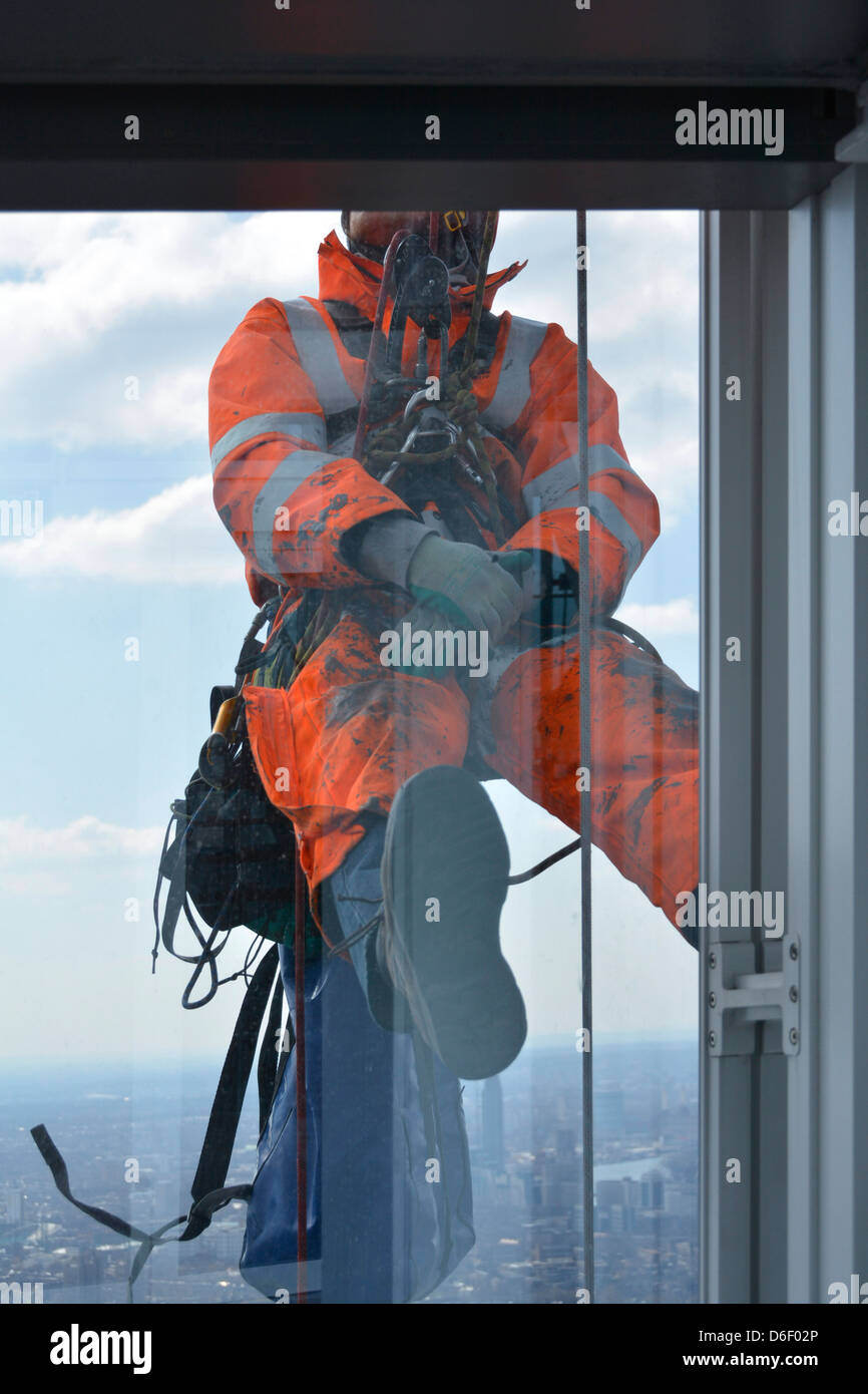 L'uomo sospeso su corde sulla faccia esterna di una torre di Londra edificio a blocco di effettuare lavori di manutenzione alla vetratura Foto Stock