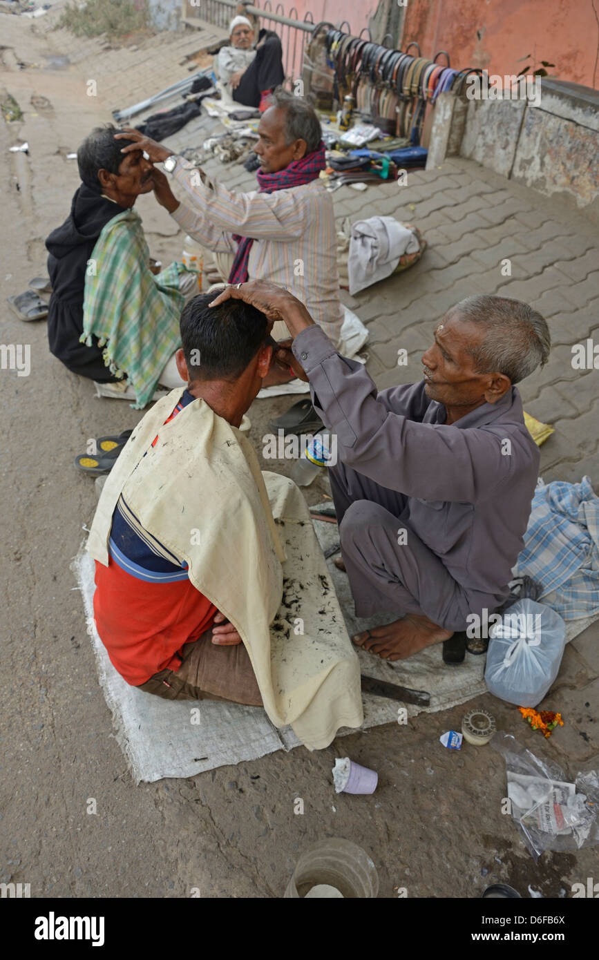 Un barbiere che dà al suo cliente una rasatura bagnata tra una fila di barbieri che squattano in una strada nella vecchia Delhi, India. Foto Stock