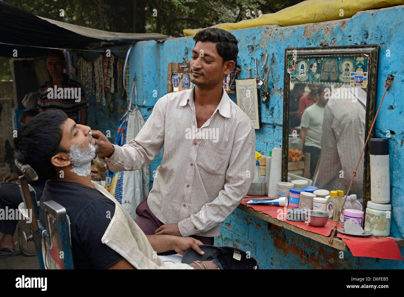 Un marciapiede barbiere dando il suo cliente una rasatura in una stretta strada di Vecchia Delhi in India Foto Stock