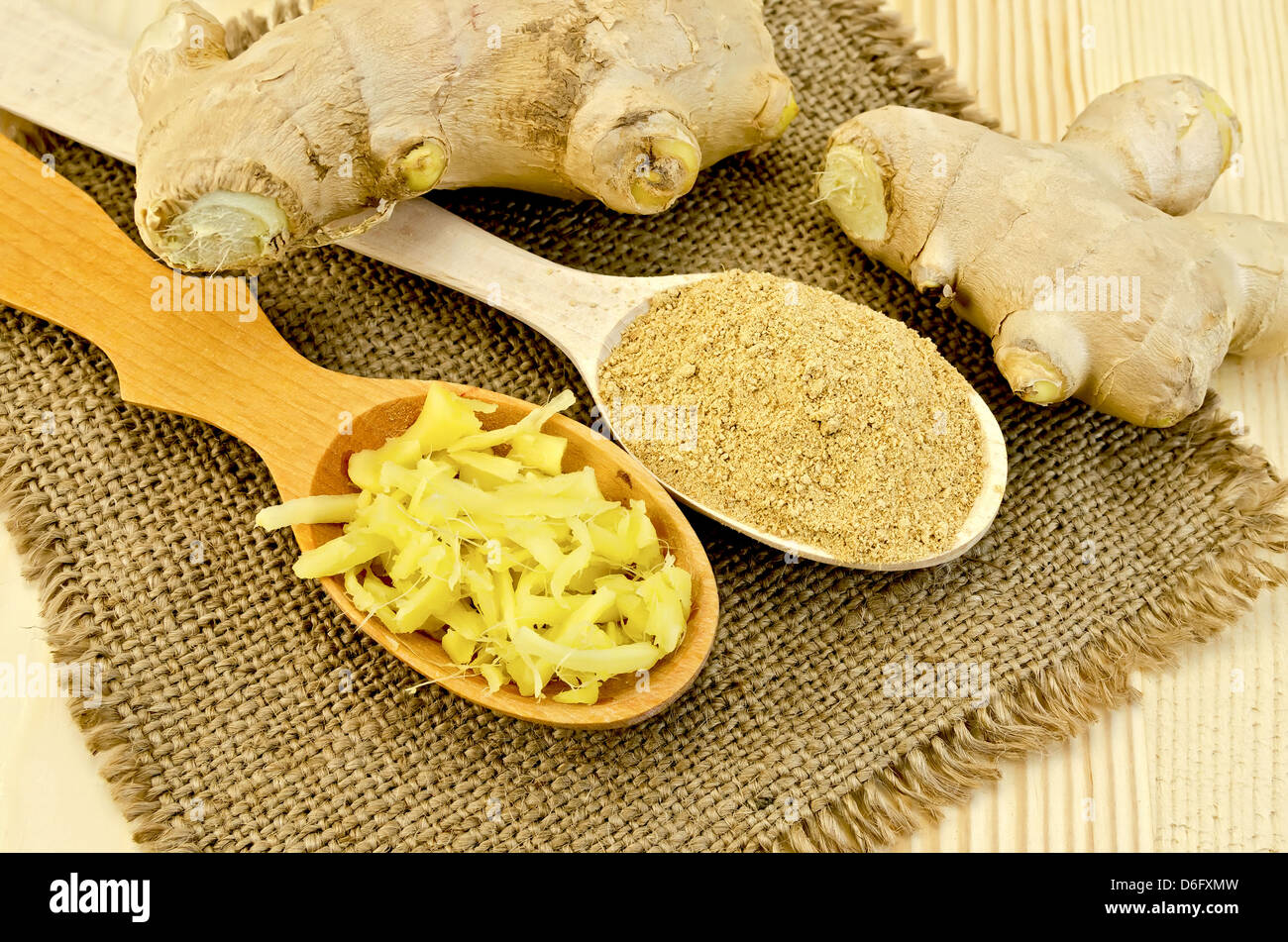 Due cucchiai di legno di polvere e lo zenzero grattugiato, radice di zenzero su un tovagliolo in una tela di sfondo scheda di legno Foto Stock