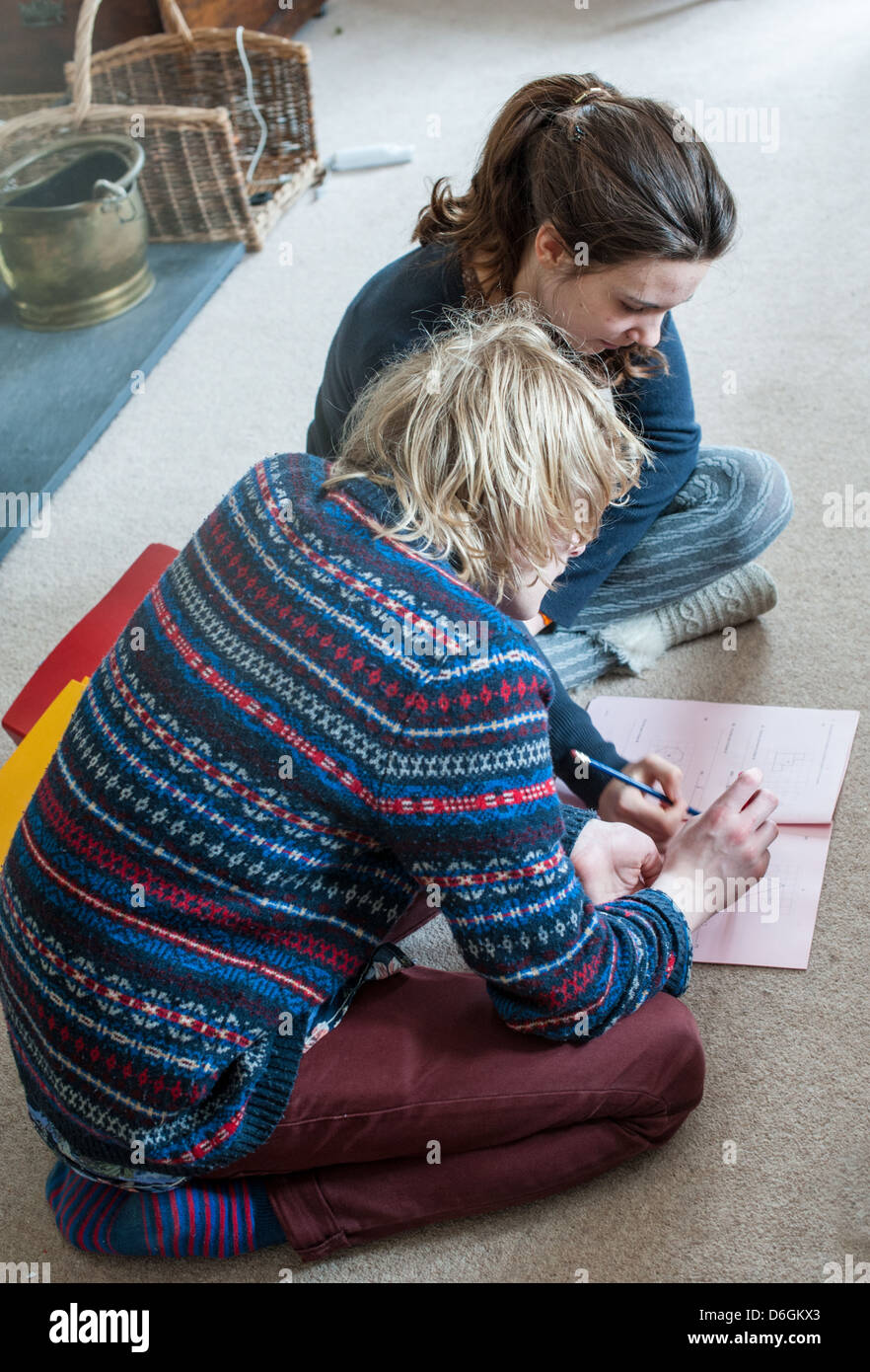 Ragazzo adolescente e la ragazza seduta su un soggiorno moquette si aiuta a vicenda con una matematica GCSE pratica di carta e di revisione per gli esami Foto Stock