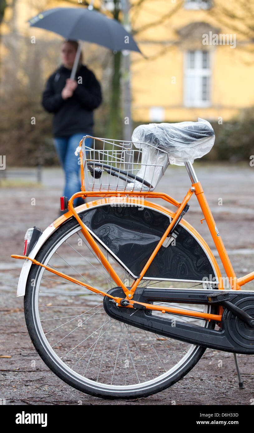 Una donna con un ombrello passeggiate passato una bicicletta con un sacchetto di plastica sulla sua sede a Osnabrück, Germania, 29 febbraio 2012. Foto: FRISO GENTSCH Foto Stock