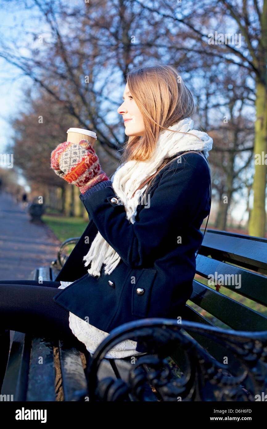 Donna con caffè su una panchina nel parco Foto Stock