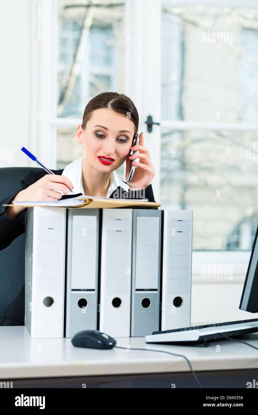 Giovane imprenditrice lavorando nel suo ufficio, si siede dietro le cartelle e sul telefono è un cliente o client Foto Stock