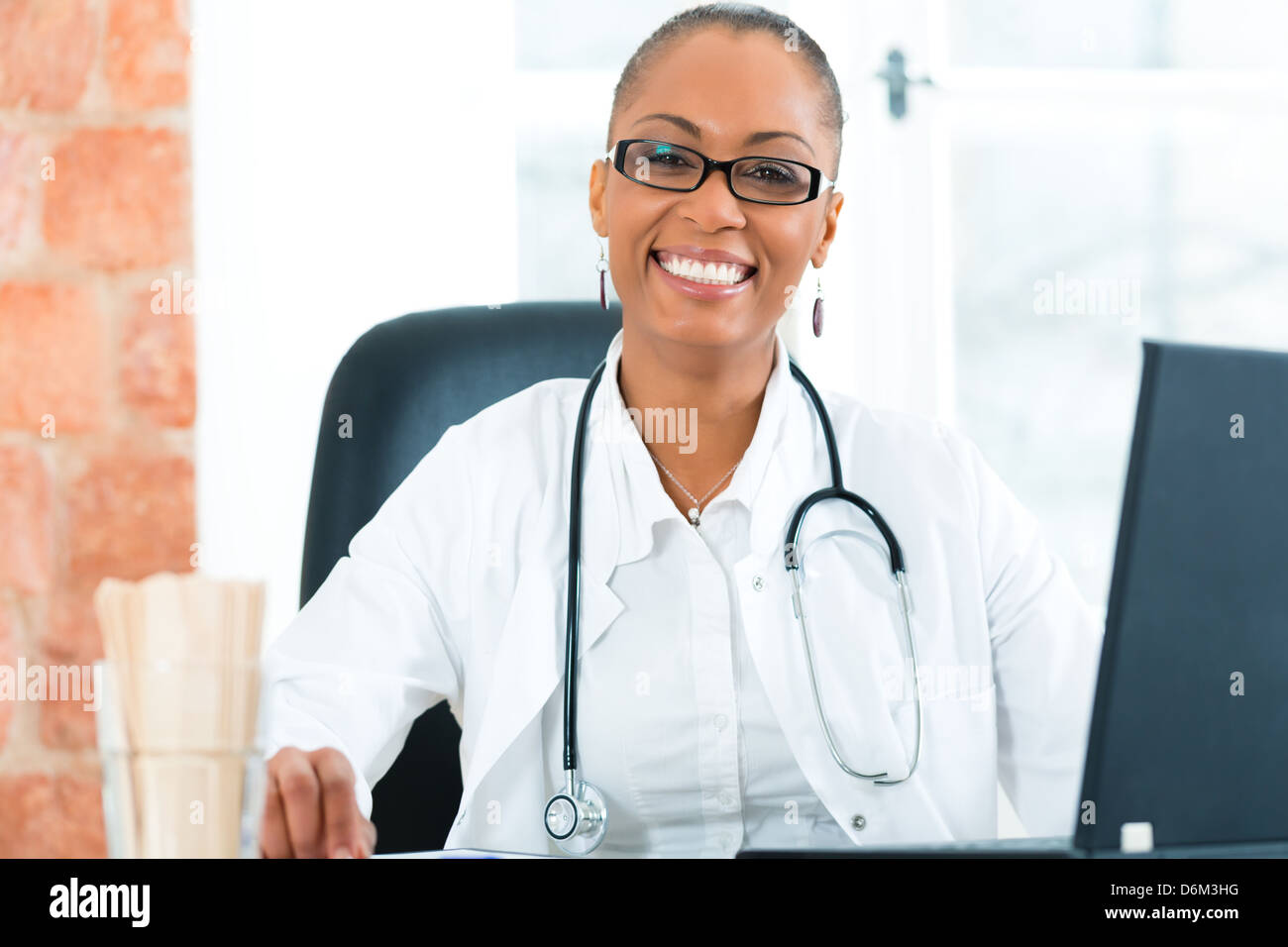 Giovane femmina nera medico seduta a una finestra nella clinica, ha uno stetoscopio Foto Stock