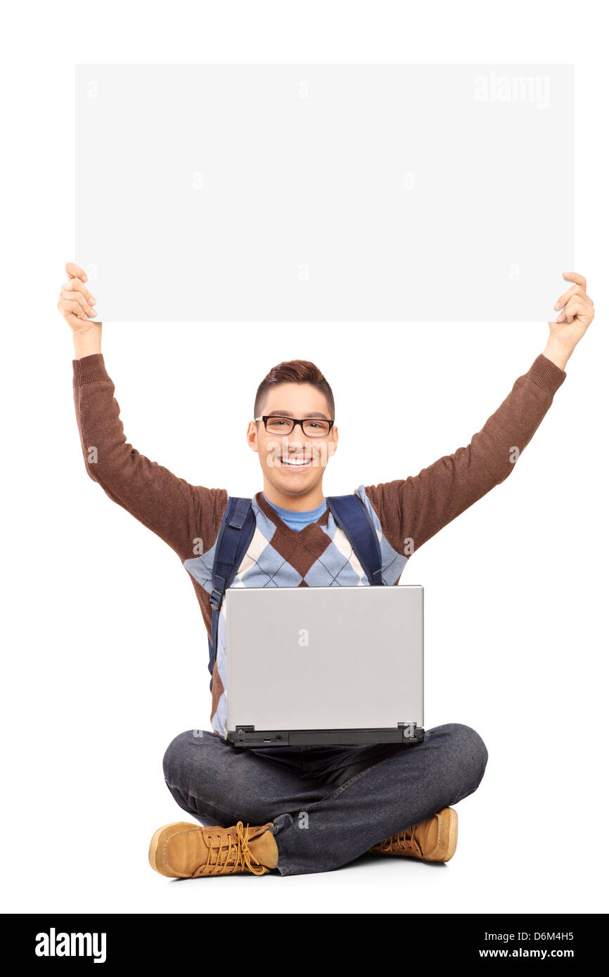 Maschio sorridente studente seduto con laptop e tenendo un pannello vuoto, isolato su sfondo bianco Foto Stock