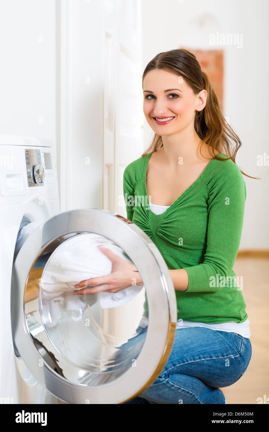 Giovane donna o governante ha bucato giornata a casa, lei prende il fuori della lavatrice o della asciugatrice Foto Stock