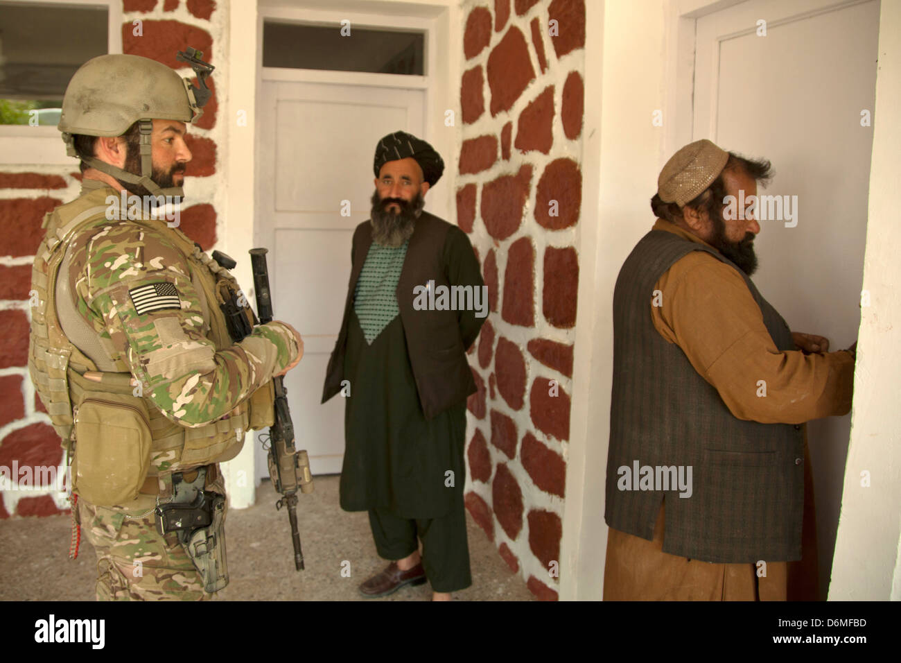 Una delle forze speciali degli Stati Uniti soldato e il governatore di distretto di attendere per una clinica per aprire durante una pattuglia con l esercito nazionale afgano forze speciali Aprile 14, 2013 nella provincia di Helmand, Afghanistan. Foto Stock