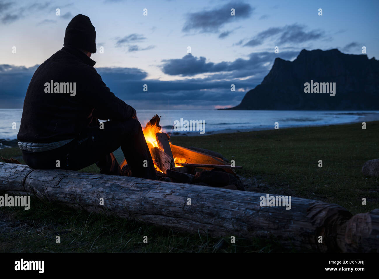 L uomo si siede a sera falò a Utakleiv beach, Isole Lofoten in Norvegia Foto Stock