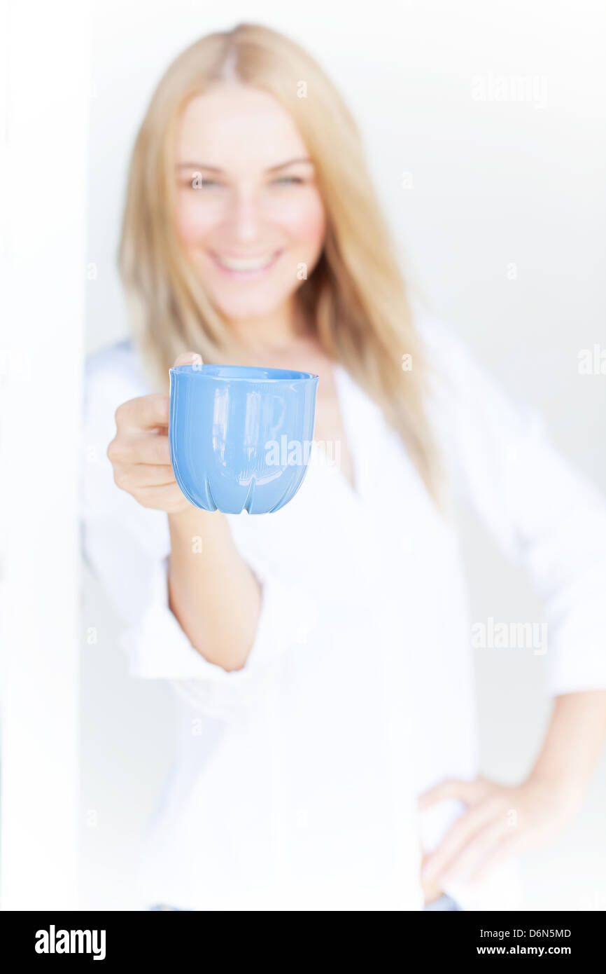 La sfocatura di immagine carina ragazza bionda tenere blu tazza di caffè su sfondo bianco, mattina bere, il concetto di felicità Foto Stock