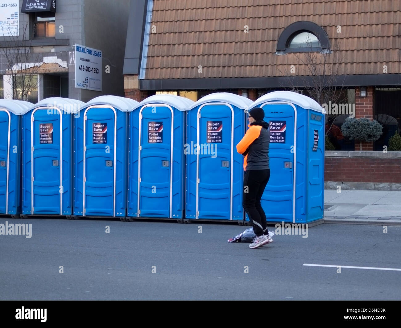 Un runner salta in alto e in basso e tenere in caldo mentre si è in attesa per un bagno portatile al 2013 Toronto Yonge Street 10K run Foto Stock