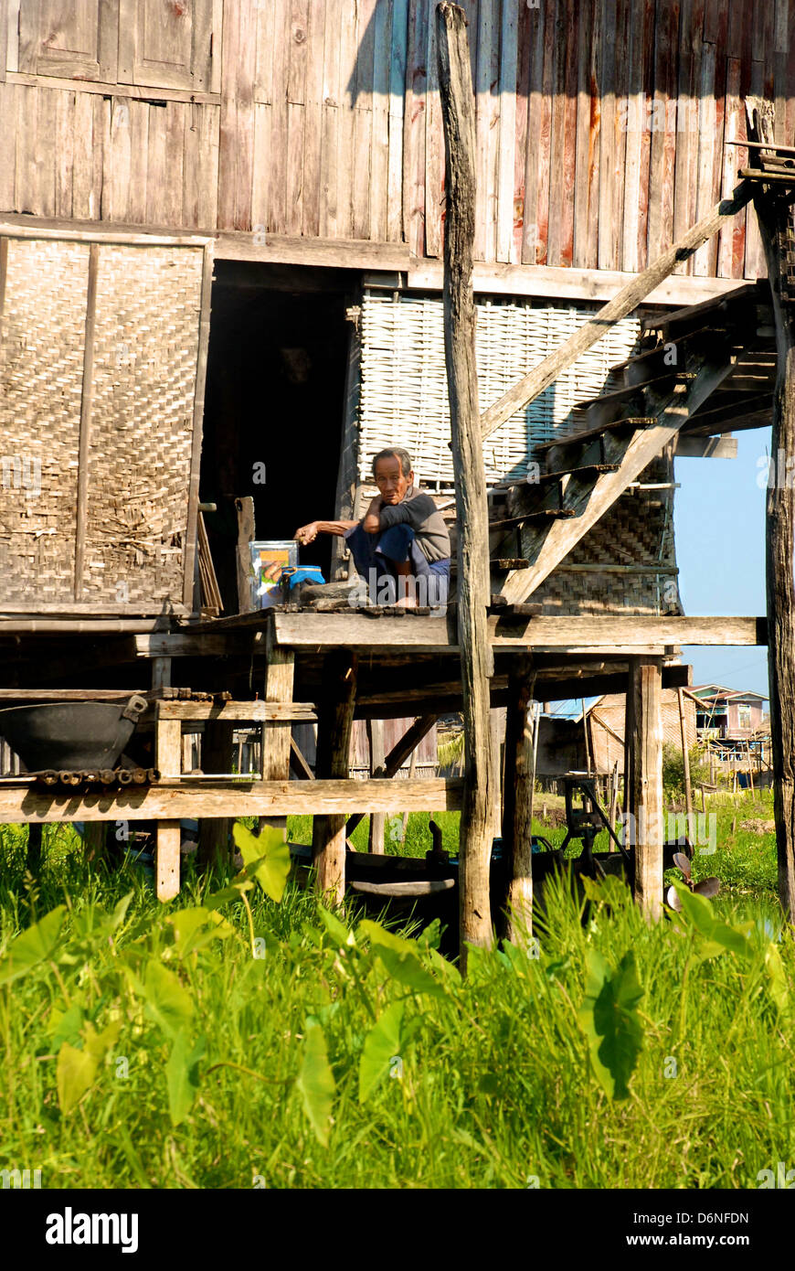 Uomo seduto sulle scale sulla casa costruita su palafitte sopra l'acqua, Lago Inle, Birmania, Mayanmar Foto Stock