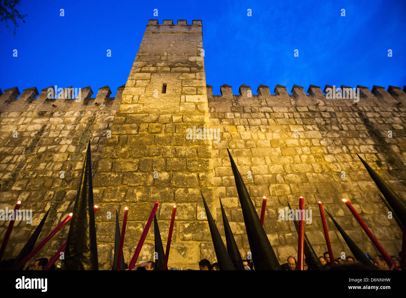 Siviglia, Spagna, cappucci conici e candele di fronte le mura fortificate di Alcazar di Siviglia per la Semana Santa Foto Stock