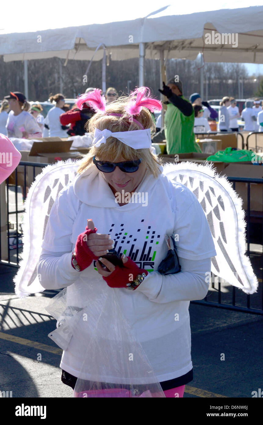 Runner in Angel Wings utilizza il telefono cellulare a warm-up rally per 5k gara. Foto Stock