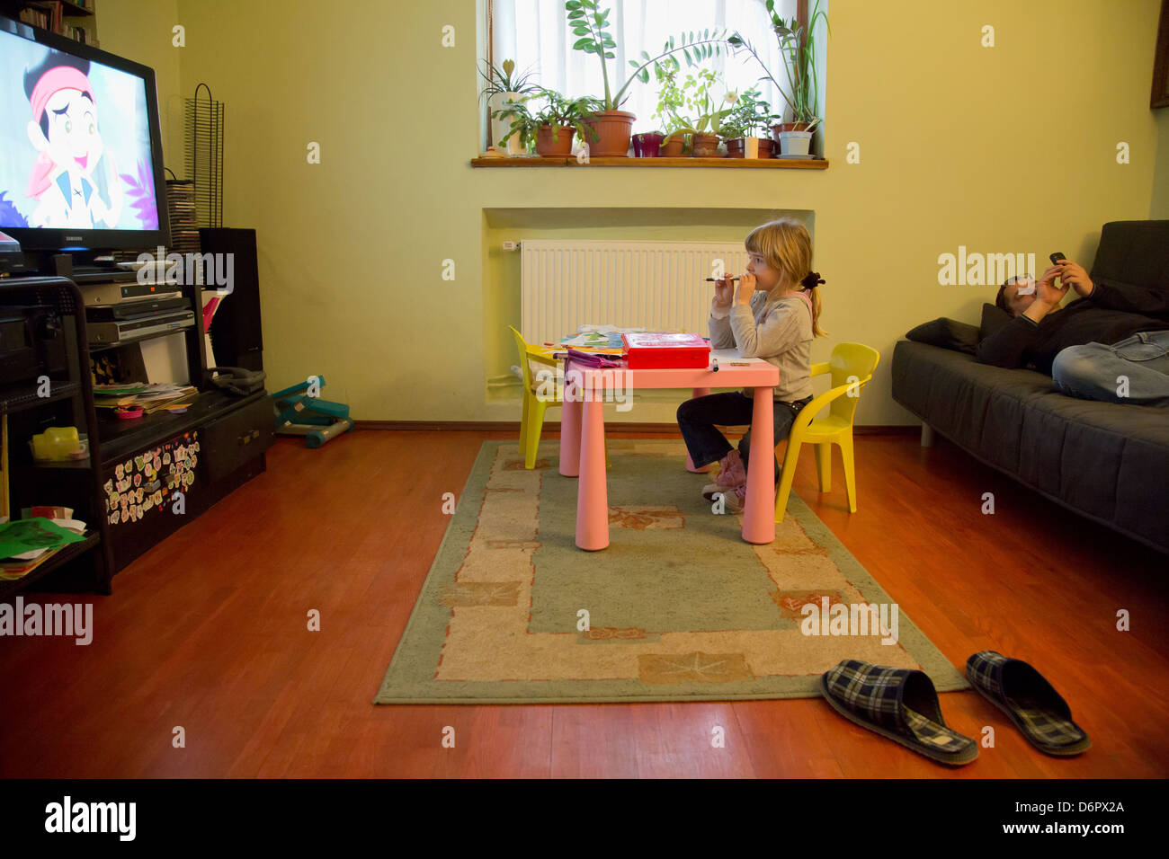 Wroclaw, Polonia, una ragazza guarda una serie animata in televisione e suo padre sdraiato sul divano Foto Stock