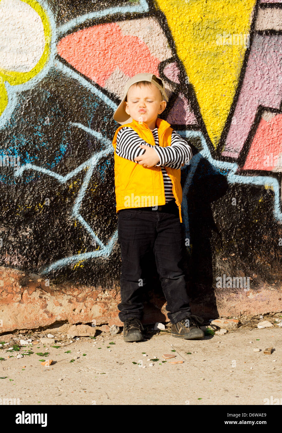 Maliziosa little boy in piedi in posa di fronte delle colorate di graffiti su un muro il raggrinzimento le sue labbra come se per chiedere o dare un bacio. Foto Stock