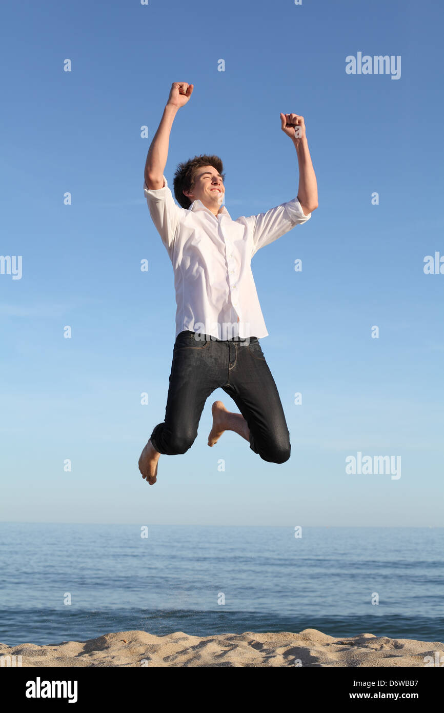 Boy jumping happy sulla spiaggia con il mare e con un cielo blu in background Foto Stock