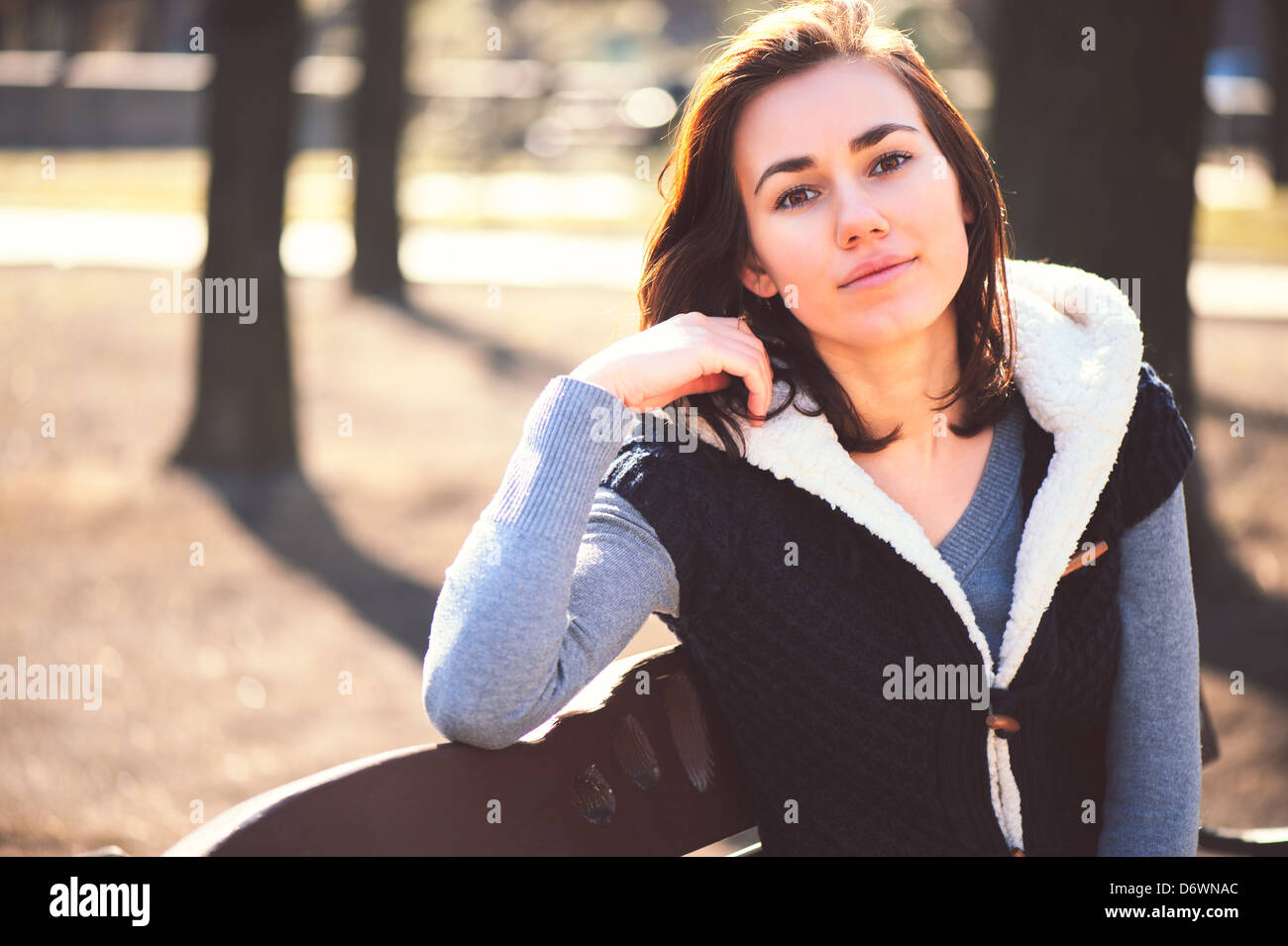 Ritratto di giovane ragazza seduta su una panchina nel parco di primavera nella giornata di sole Foto Stock