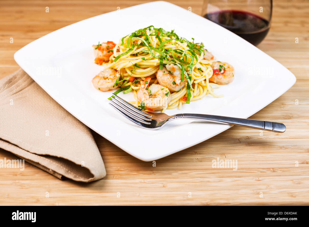 Closeup foto orizzontale di un piatto di pasta con focus su gamberi grandi in acciaio inossidabile forcella, basilico, panno assorbente e vino rosso Foto Stock
