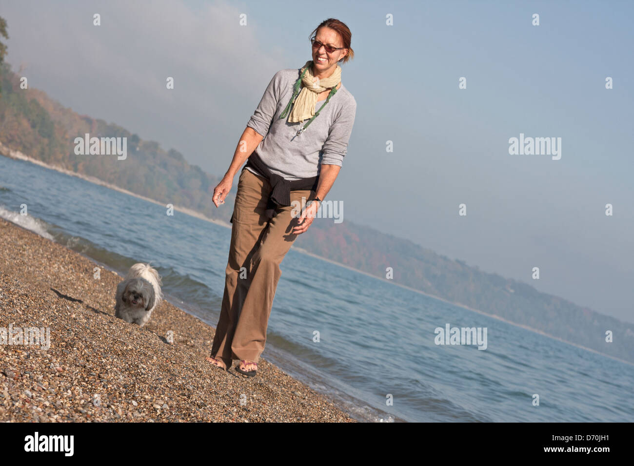 Una donna e il suo cane a camminare su un lago MIchigan spiaggia su una soleggiata giornata autunnale. Foto Stock