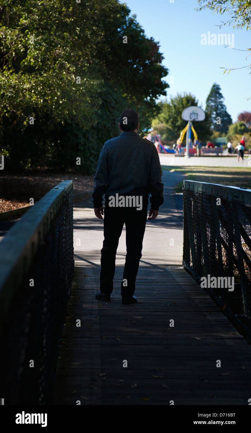 Vista posteriore di un uomo in un parco a piedi verso un parco giochi per bambini. Foto Stock