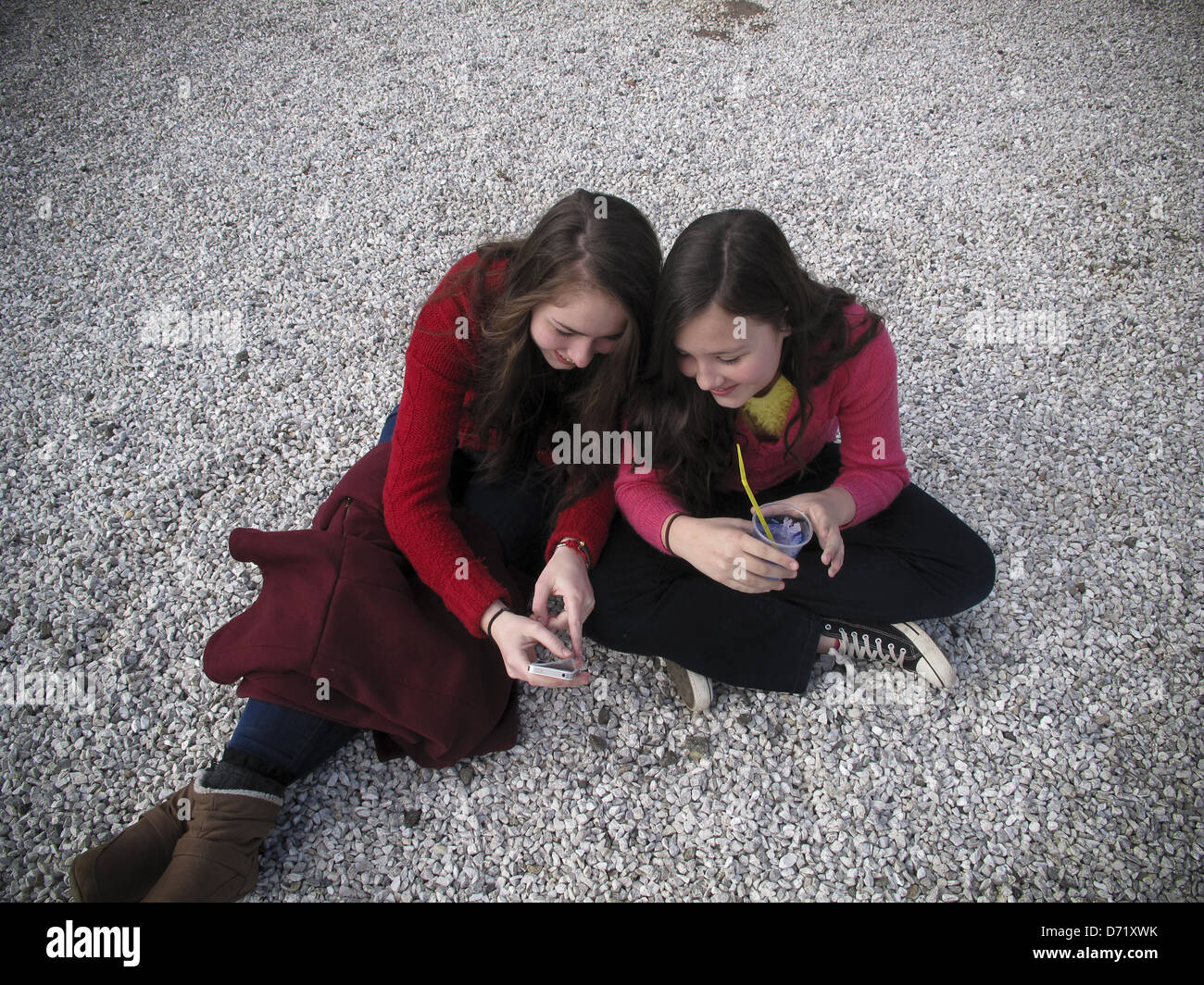 Due ragazze seduta sul terreno con iPhone e bere Foto Stock