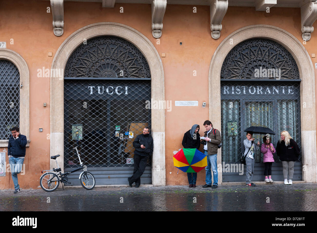 La gente si ripara dalla pioggia sotto gli ombrelloni a buon mercato in Piazza Navona, Roma, Italia Foto Stock