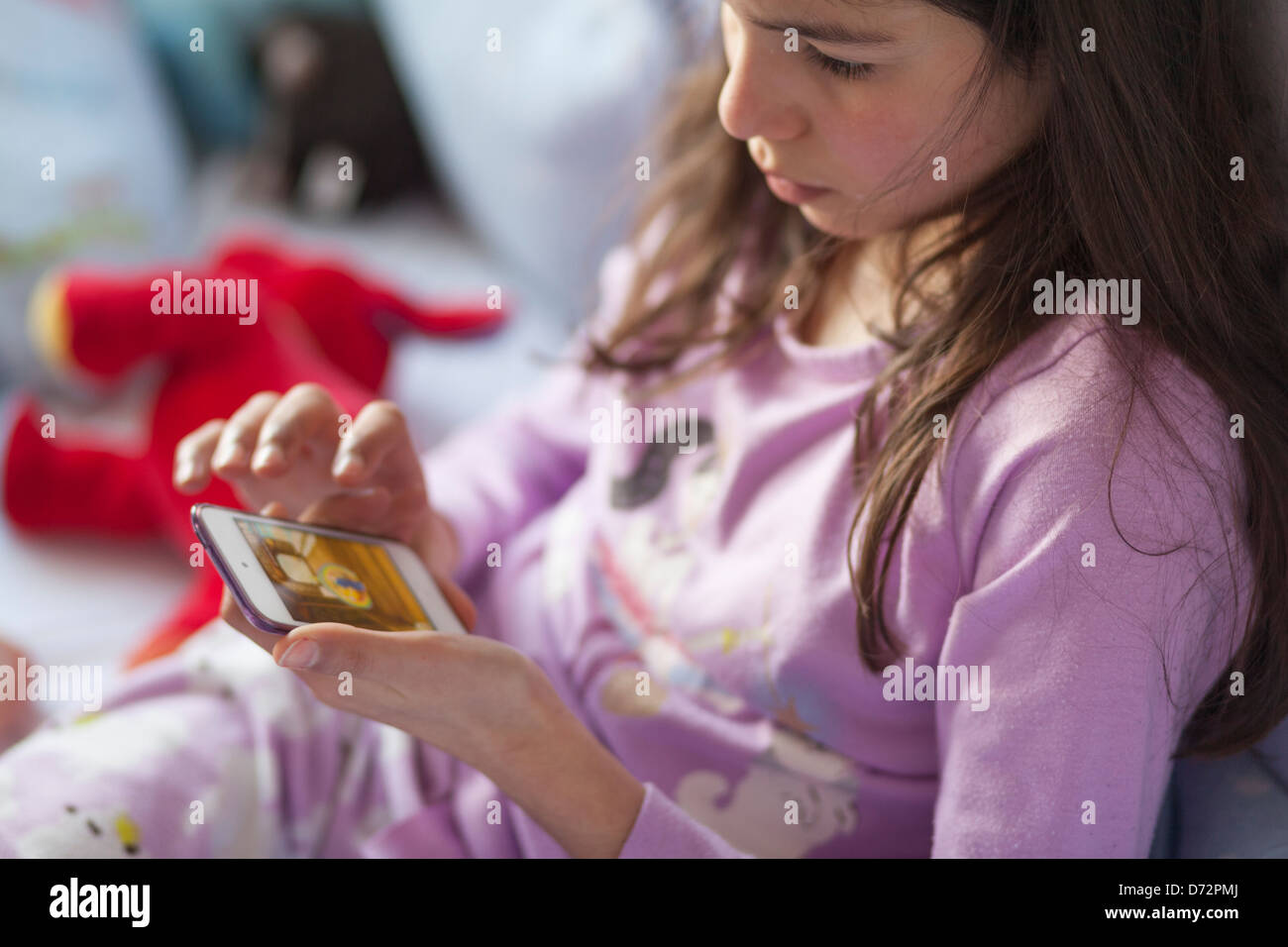 Ragazza giovane gioca sul dispositivo mobile a letto Foto Stock