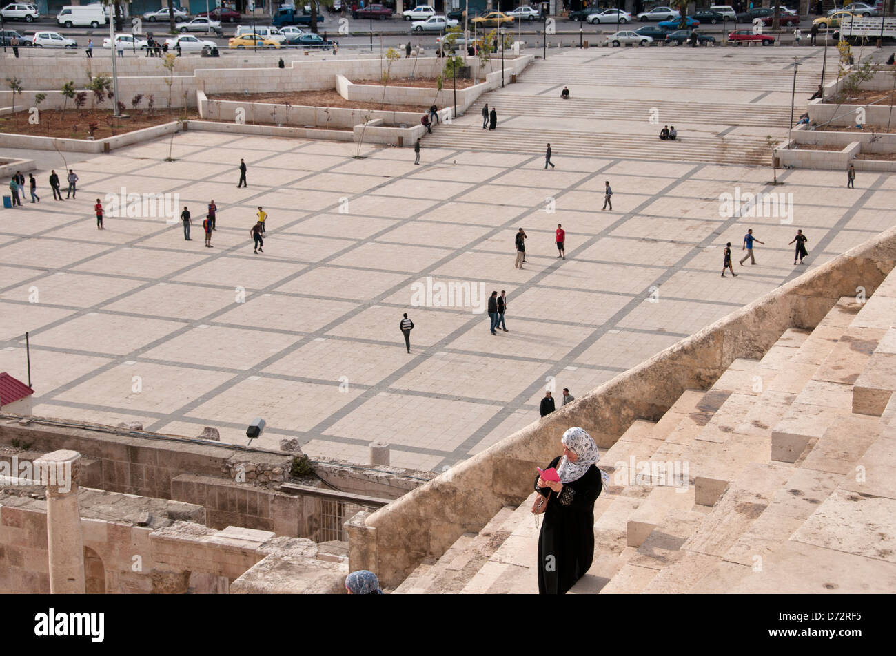 Giordania, ad Amman. Anfiteatro Romano. Donna che guarda il suo cellulare mentre i ragazzi giocare a calcio in background. Foto Stock