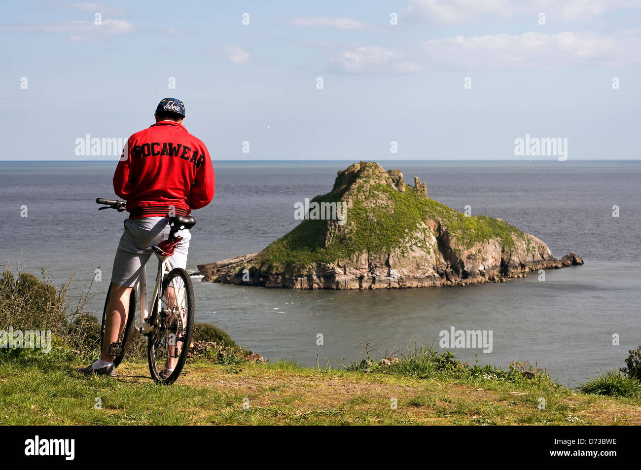 Uomo in rosso in mountain bike che si affaccia su vista della Thatcher Rock, un popolare luogo di bellezza in Torquay, Torbay,Devon, Regno Unito,rocawear Foto Stock