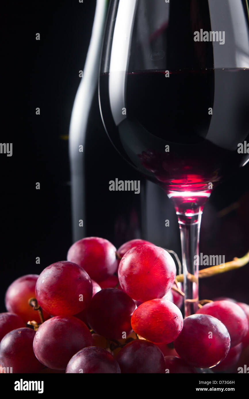 Uva e vetro con vino rosso su sfondo nero Foto Stock