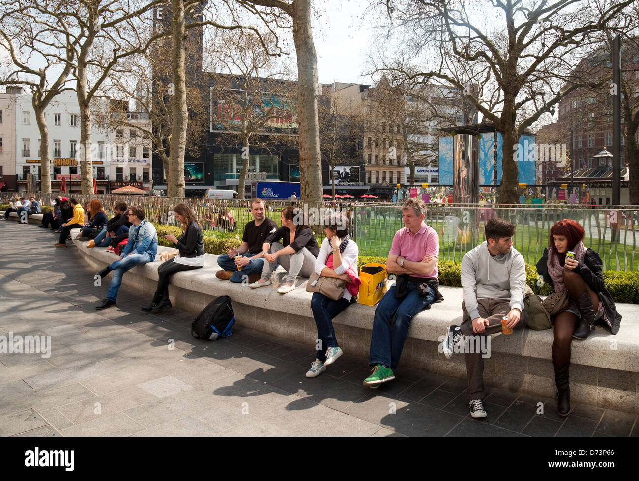 La gente seduta godendo il sole in primavera, Leicester Square, Central London WC2, Regno Unito Foto Stock