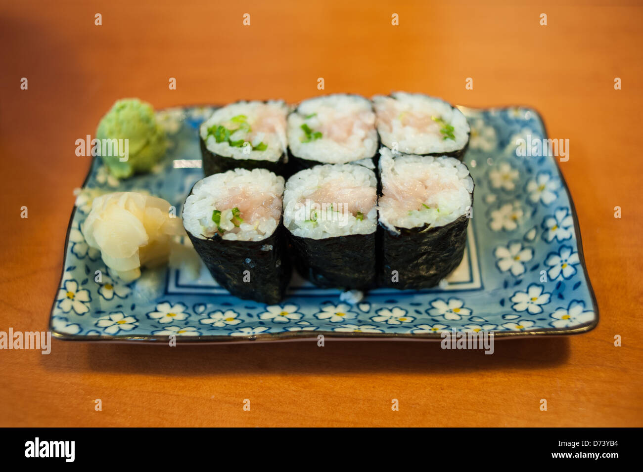 Due righe di sushi di tonno servita su una piastra blu contro un tavolo. Studio shot. Foto Stock