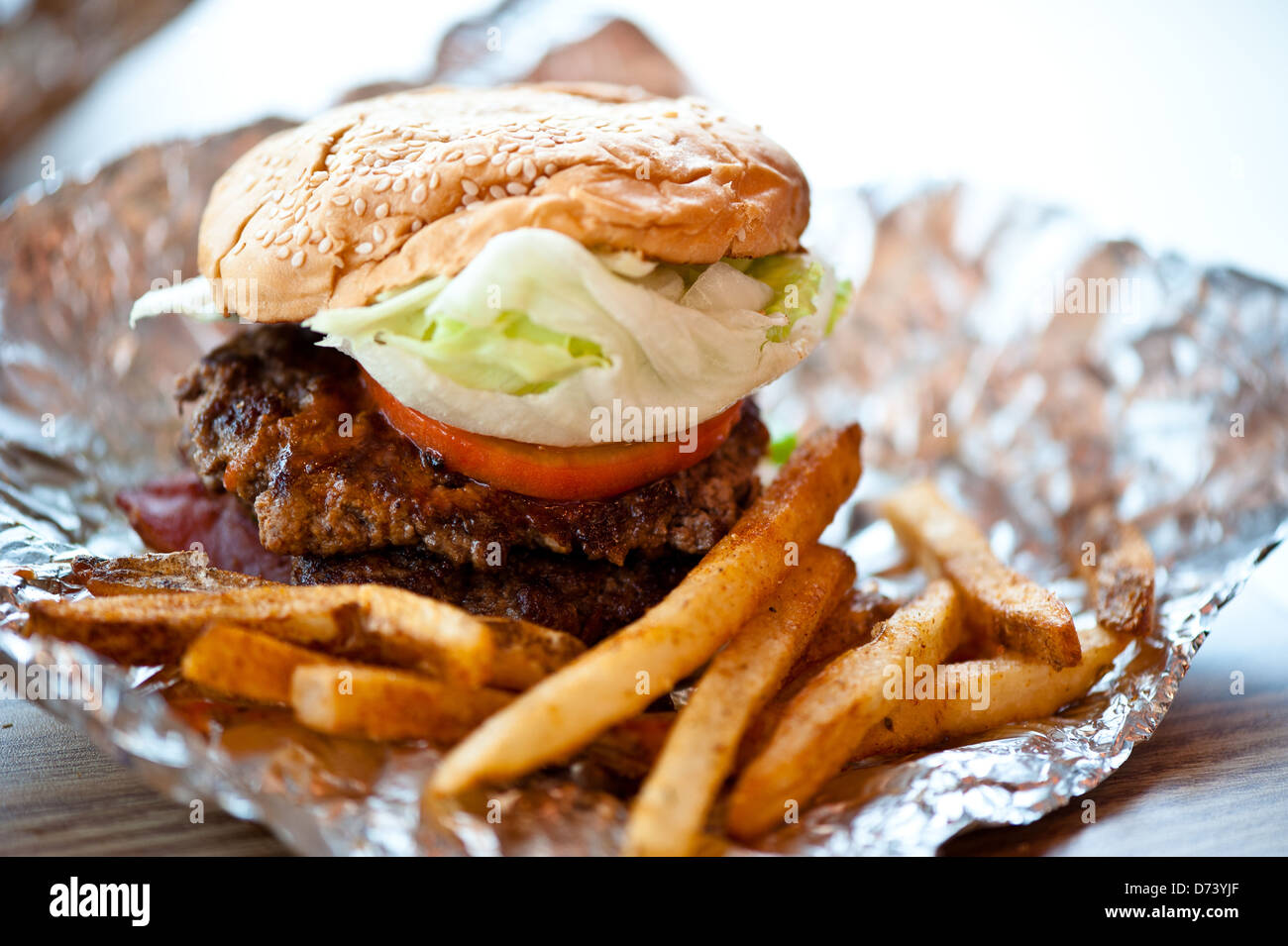 Inquadratura ravvicinata di un burger con doppia polpetta di carne di manzo, pomodori e lattuga. Servita con alcuni cajun patate fritte. Foto Stock