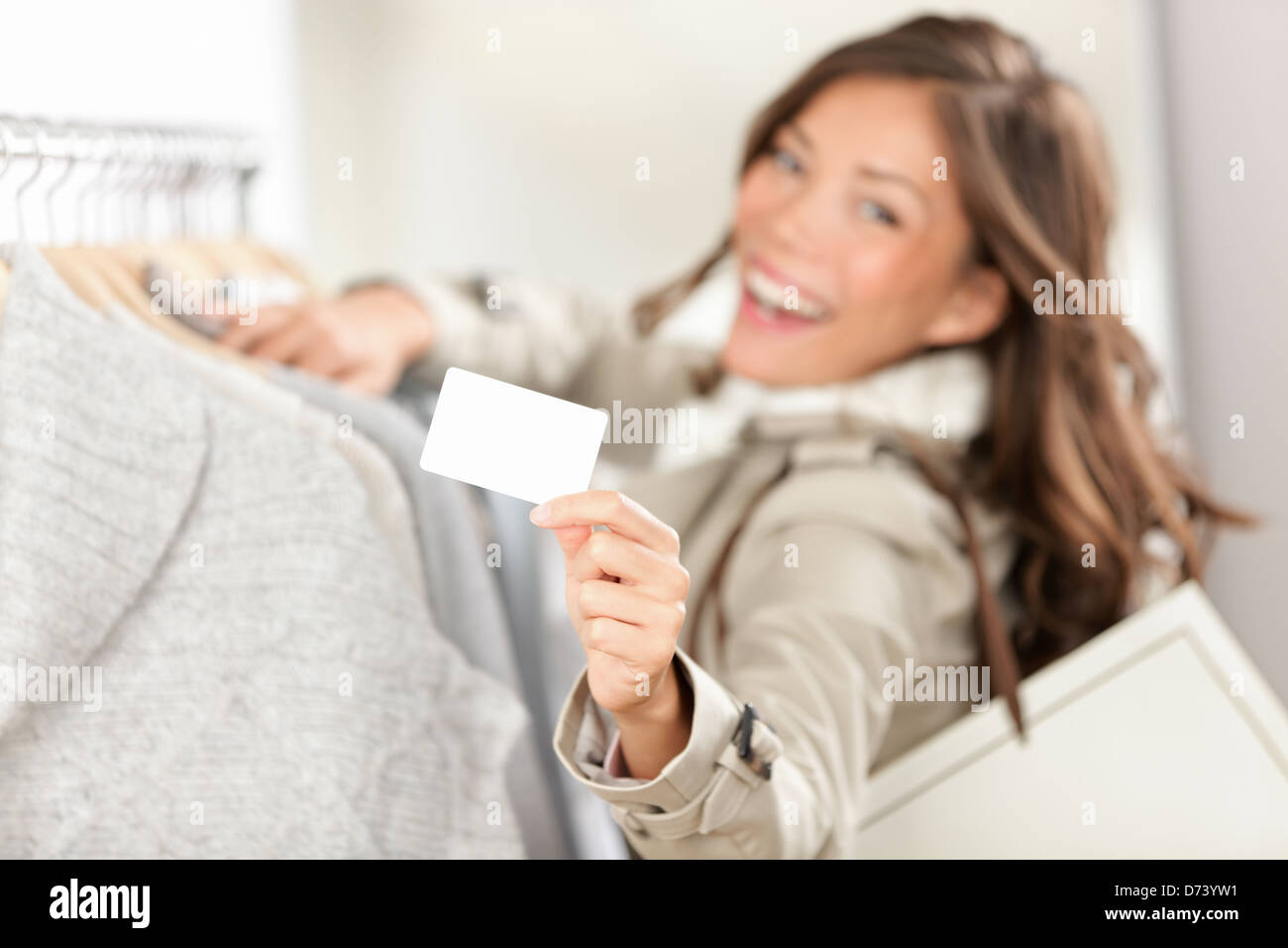 Gift Shopping Card segno. Donna shopper mostra vuoto segno bianco nel negozio di abbigliamento. Bella eccitato sorridente asian caucasian modello femminile. Foto Stock