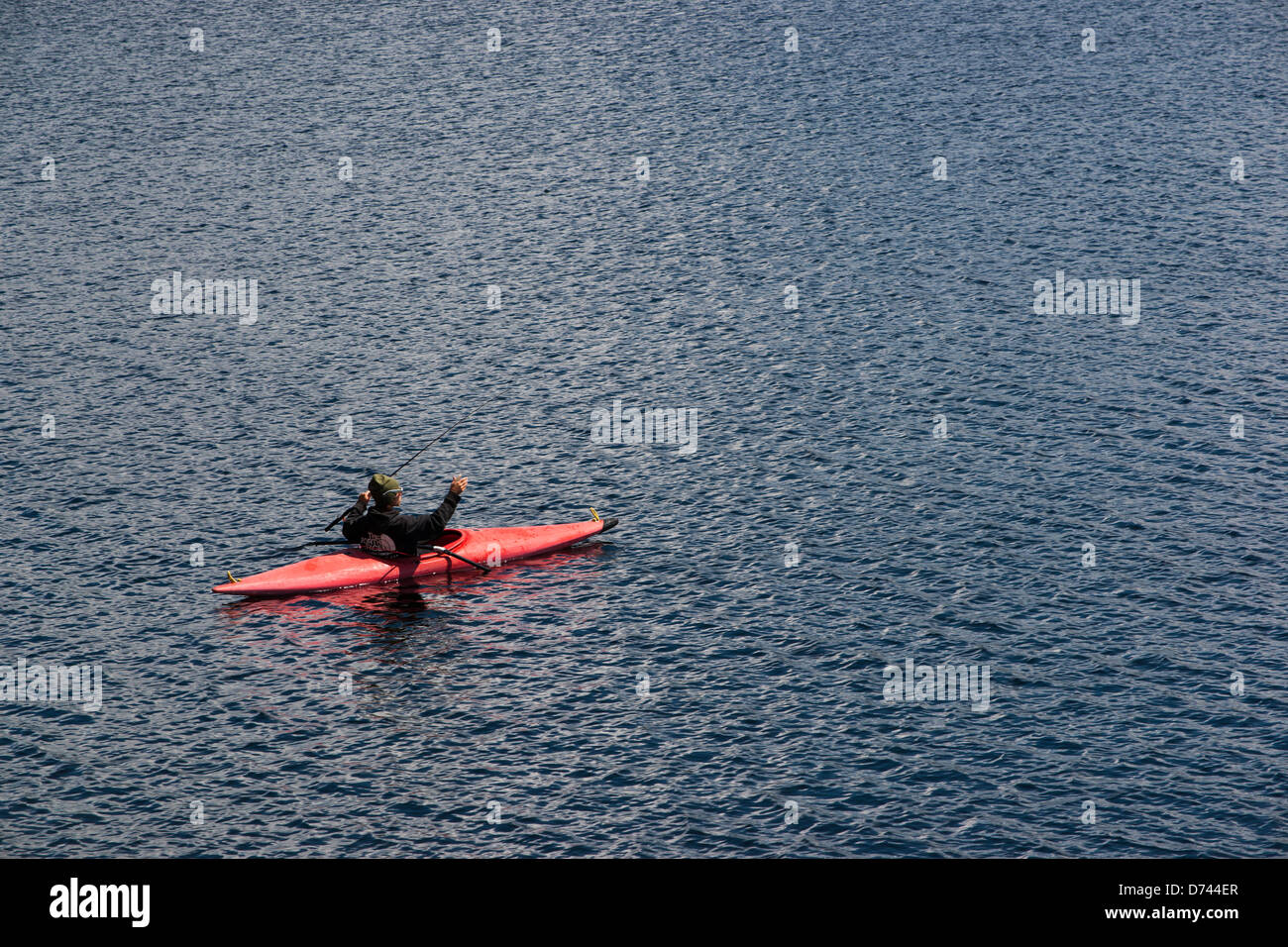 Un uomo è visto mentre la pesca da un kayak rosso in un lago con profondo blu dell'acqua. Denver, Colorado. Foto Stock