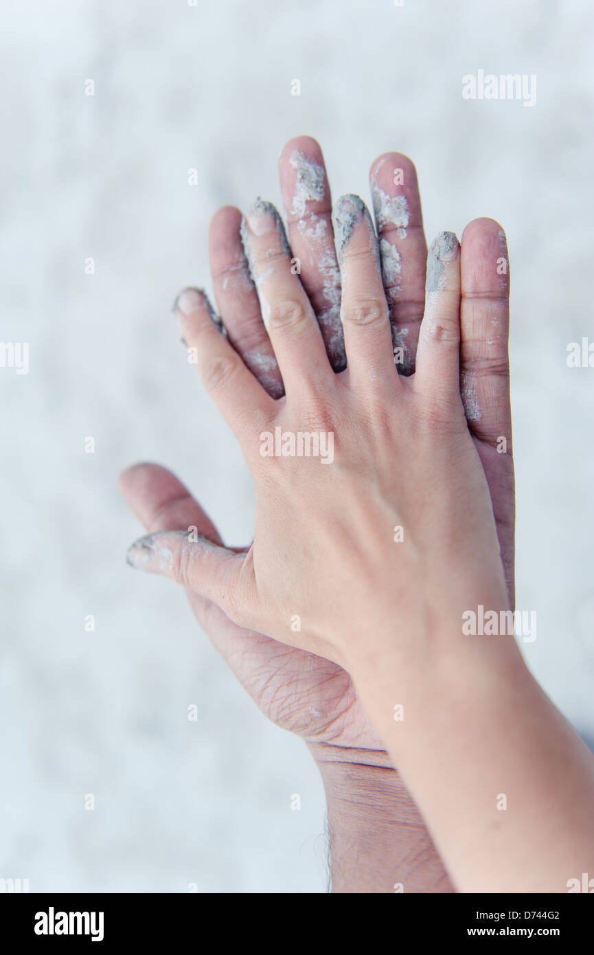 Un uomo e una donna mani toccano, coperte in bianco grigio argilla. Foto Stock