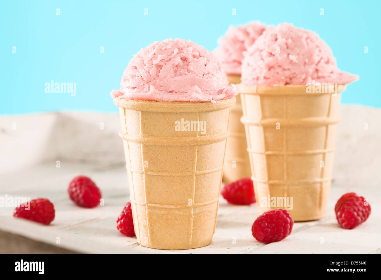 Gelato al lampone in una cialda in legno bianco e sfondo blu Foto Stock