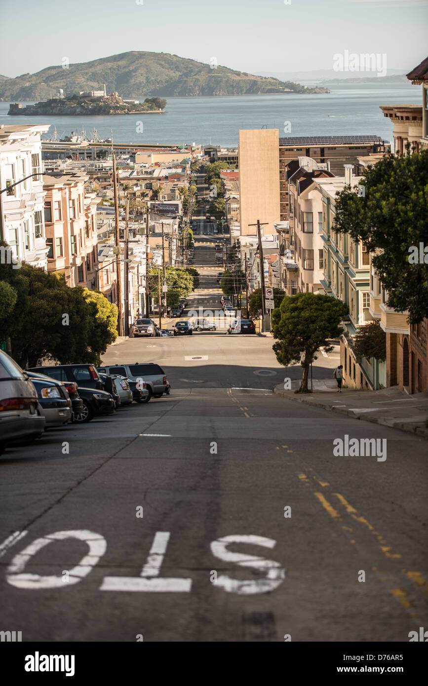 Taylor Street Ripide Hill Alcatraz View San Francisco California // SAN FRANCISCO, California - Taylor Street scende ripida attraverso il quartiere North Beach di San Francisco, offrendo vedute verso l'Isola di Alcatraz e la Baia di San Francisco. La strada è tra le strade più ripide della città che caratterizzano il terreno collinare di San Francisco. North Beach, situata sul lungomare settentrionale, è ampiamente conosciuta come il quartiere italo-americano della città e centro storico della cultura Beat Generation. L'isola di Alcatraz, visibile in lontananza attraverso la baia, servì come prigione federale dal 1934 al 196 Foto Stock