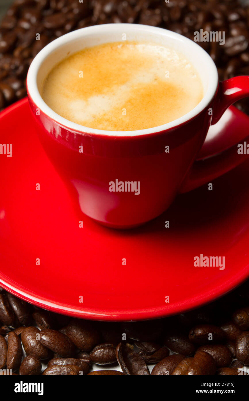 Caffè espresso in un bicchiere di rosso e piattino con fresco intero di chicchi di caffè in background, England, Regno Unito Foto Stock