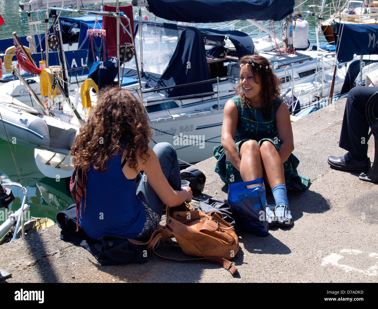 Due giovani donne sedeva al sole sulla banchina, Padstow, Cornwall, Regno Unito 2013 Foto Stock